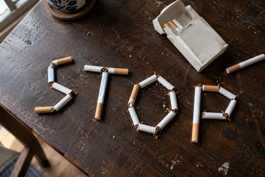 Broken cigarettes spelling the word STOP on a wooden table beside an open cigarette pack